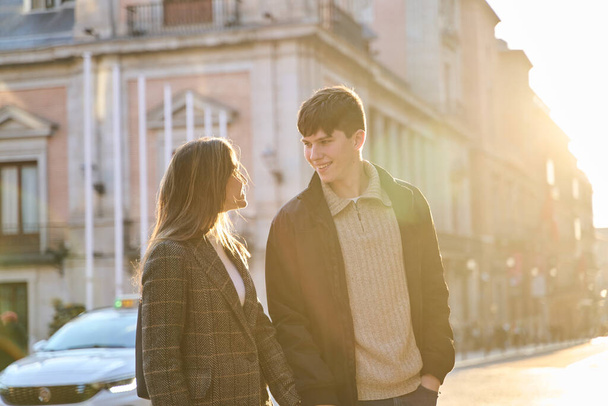 Hand in Hand spaziert das junge Paar mit der Sonne im Hintergrund durch die Stadt - Foto, Bild