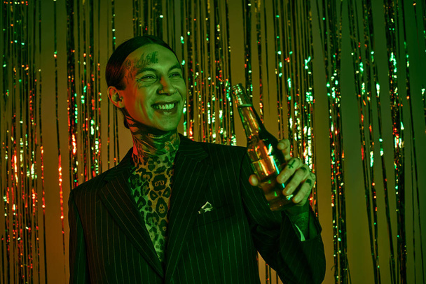 Na imprezie, facet w garniturze i krawacie trzyma butelkę - Zdjęcie, obraz