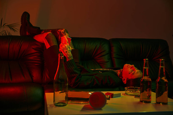 Άνδρας ξαπλωμένος σε έναν καναπέ δίπλα σε ένα τραπέζι σε ένα δωμάτιο - Φωτογραφία, εικόνα