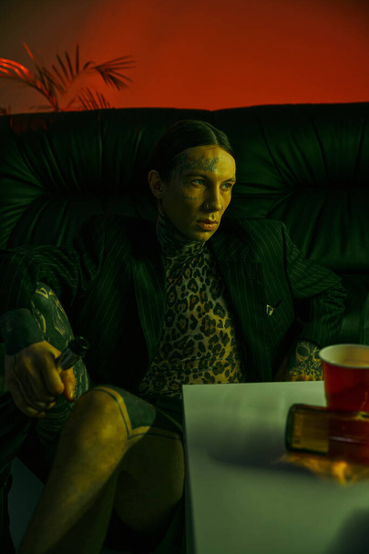 Ένας άντρας κάθεται σε έναν καναπέ δίπλα σε ένα κόκκινο κύπελλο. - Φωτογραφία, εικόνα