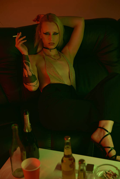 Μια γυναίκα κάθεται στον καναπέ, καπνίζοντας ένα τσιγάρο. - Φωτογραφία, εικόνα