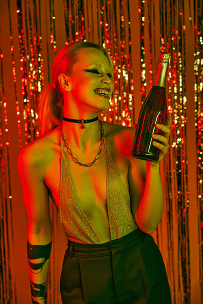 Μια γυναίκα κρατώντας ένα μπουκάλι στο χέρι της σε ένα ζωντανό rave party ή νυχτερινό κέντρο διασκέδασης - Φωτογραφία, εικόνα