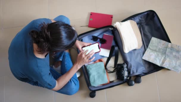 Топ-вид женщины, пользующейся смартфоном во время хранения вещей в чемодане перед поездкой - Кадры, видео