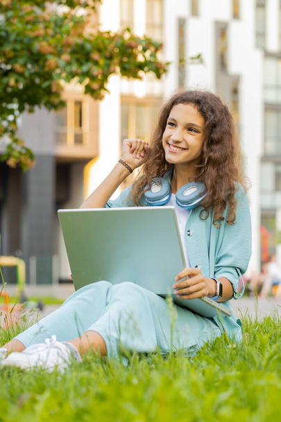 Happy preteen child kid with laptop scream in delight raise hands in triumph winner gesture celebrate success win money in lottery. Excited girl sitting on grass in city park get online good news - Photo, Image