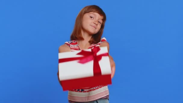 Lovely smiling young preteen child girl kid presenting birthday gift box stretches out hands, offer wrapped present career bonus, celebrating party. Little cute children on studio blue background - Footage, Video