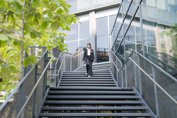 Professional woman in suit walks down steps outside a modern office building - Fotó, kép