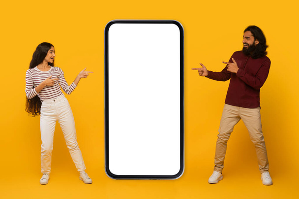 Gülümseyen adam ve kadın etkileşime girer, sarı bir zemin üzerinde boş büyük bir akıllı telefon ekranına işaret ederler. - Fotoğraf, Görsel