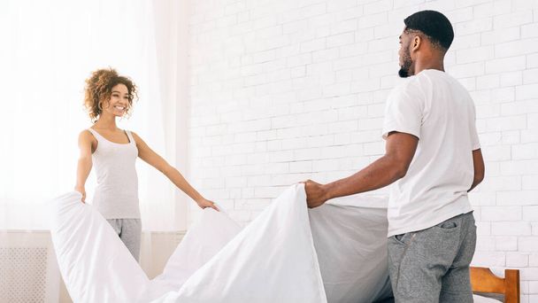 A cheerful african american couple bonding while making the bed together in a bright, airy bedroom setting - Photo, Image