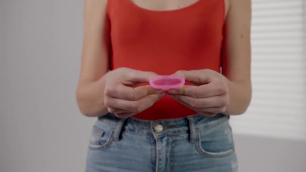 Fiatal lány kezében menstruációs csésze. Fogalma PMS. Bemutató környezetbarát termék a nők számára, latex szilikon kupa. Menstruációs egészség közelről. Újrafelhasználható higiéniai termékek gyűjteménye. Magas - Felvétel, videó