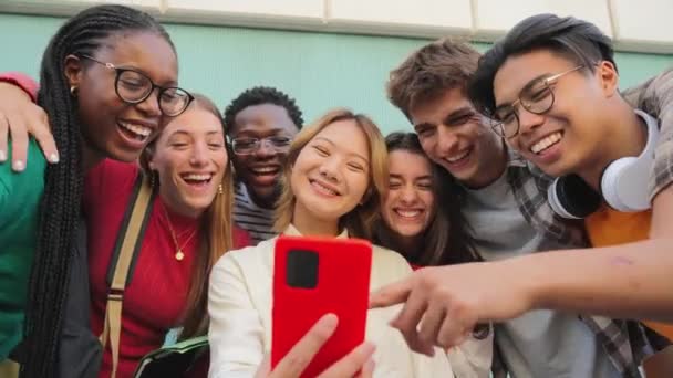 Duża grupa uśmiechniętych, wielorasowych nastolatków korzystających ze smartfonów, oglądających śmieszne filmy, robiących zakupy online, cieszących się na świeżym powietrzu. Multiethnic młodych prawdziwych ludzi dobrze się bawiących przeglądając z aplikacją na telefon komórkowy - Materiał filmowy, wideo