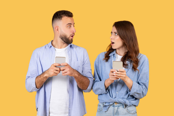 Mann und Frau zeigen schockierte Mienen, wenn sie auf ihre Smartphones schauen und alarmierende Nachrichten oder Nachrichten andeuten. - Foto, Bild