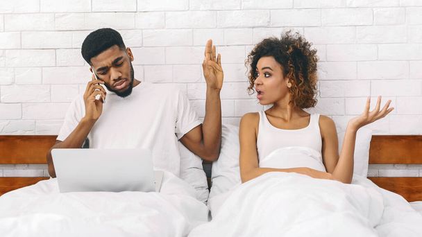 Mujer afroamericana en la cama que parece exasperada mientras su pareja habla por teléfono, ilustrando la dinámica de las relaciones - Foto, imagen