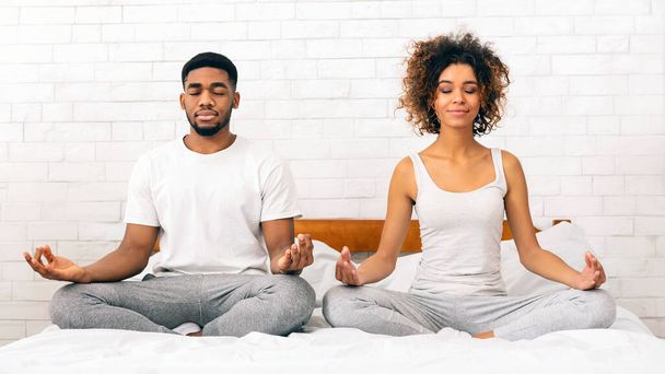 Klidný mladý africký pár praktikující meditaci spolu v klidném prostředí ložnice - Fotografie, Obrázek