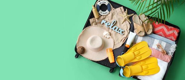 Suitcase with beach accessories and clothes on green background with space for text - Photo, Image