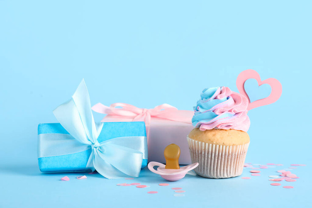 Delicious cupcake with gift boxes, pacifier and decor on blue background. Gender reveal party concept - Photo, Image