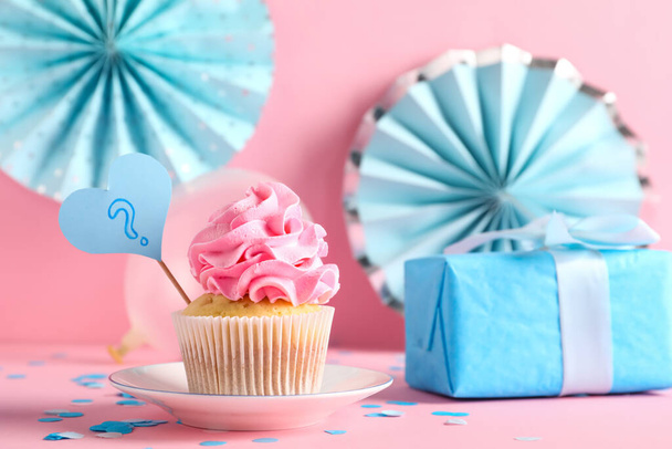 Delicioso cupcake con signo de interrogación, caja de regalo y decoraciones sobre fondo rosa. Género revelar concepto de partido - Foto, imagen