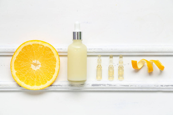 Beyaz ahşap arka planda turuncu parçalı C vitamini şişeleri ve ampules - Fotoğraf, Görsel
