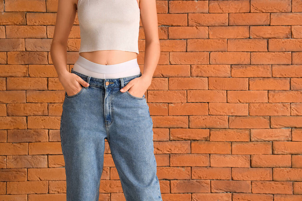 Jovem mulher em roupas de jeans elegantes perto de parede de tijolo laranja - Foto, Imagem