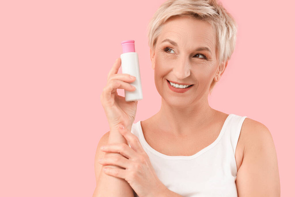 Mature woman with bottle of skincare product on pink background, closeup - Photo, Image