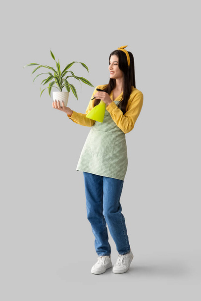 Красива молода щаслива жінка садівник обприскує воду на рослину на сірому фоні - Фото, зображення