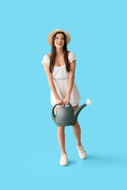 Schöne junge glückliche Gärtnerin mit Gießkanne auf blauem Hintergrund - Foto, Bild