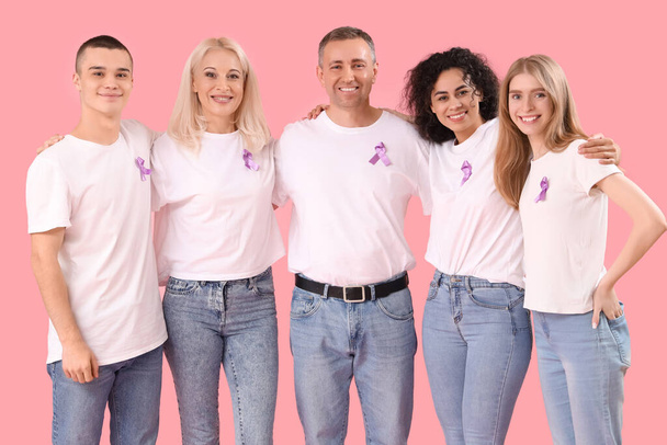 Άνθρωποι με κορδέλες ευαισθητοποίησης λεβάντας αγκαλιασμένοι σε ροζ φόντο. Παγκόσμια Ημέρα Καρκίνου - Φωτογραφία, εικόνα