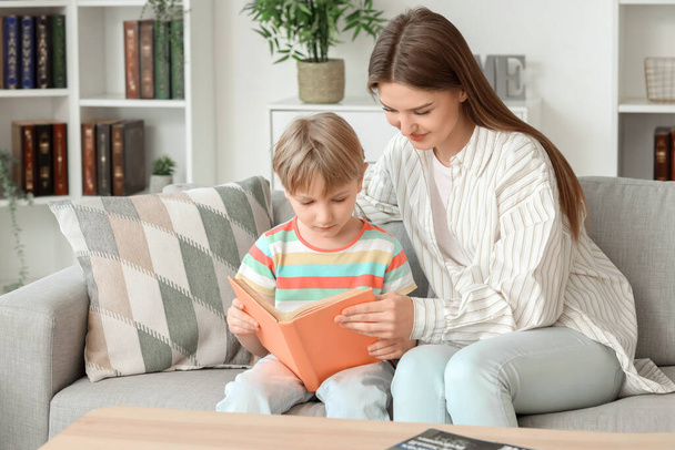 Mały chłopiec z matką czytający książkę na sofie w domu - Zdjęcie, obraz