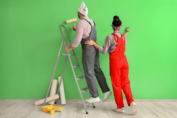 Beau jeune couple avec rouleau de peinture et brosse près du mur vert faisant la réparation dans la maison neuve - Photo, image