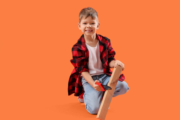 Милый маленький строитель пилит деревянную доску на оранжевом фоне - Фото, изображение
