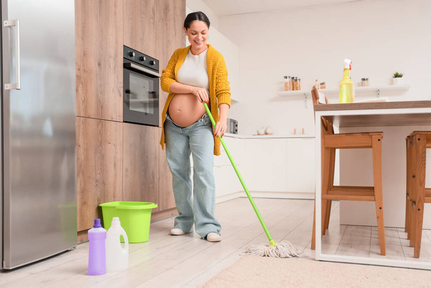Genç hamile kadın mutfakta yerleri paspaslıyor. - Fotoğraf, Görsel