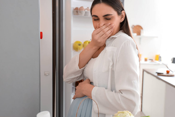 Молодая беременная женщина плохо пахнет из холодильника на кухне - Фото, изображение