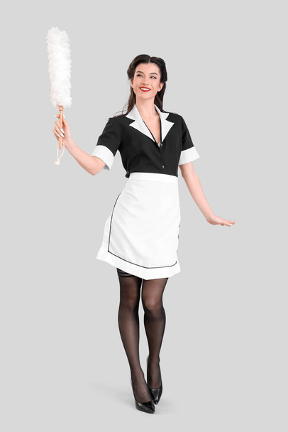 Beautiful pin-up chambermaid with dust brush on grey background - Photo, Image