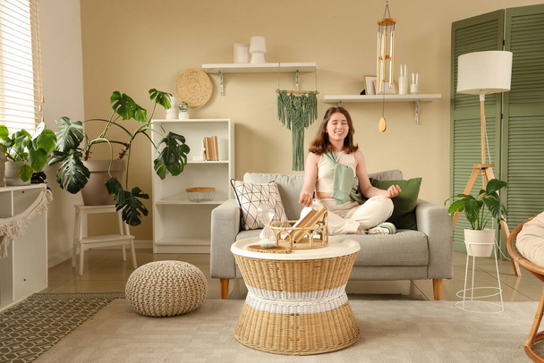 Mladá žena medituje na pohovce a zavěšení zvonek v obývacím pokoji - Fotografie, Obrázek