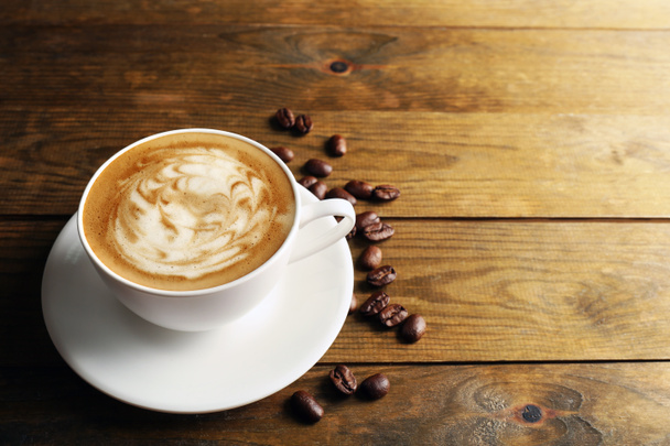 kopje koffie latte kunst met korrels op houten achtergrond - Foto, afbeelding