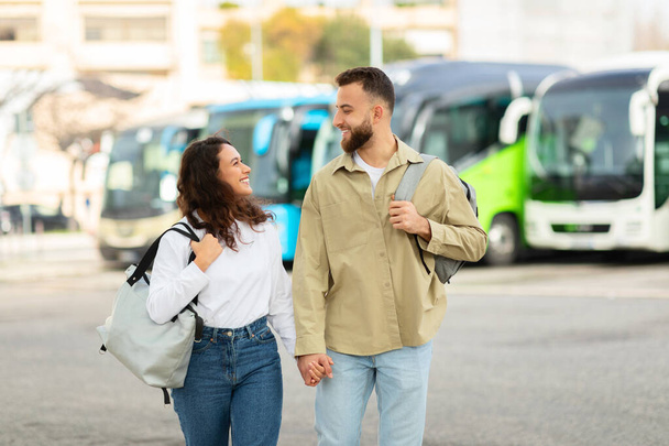 Una pareja feliz charlando y llevando mochilas en una estación de autobuses proporcionan un concepto de viaje y compañía - Foto, imagen