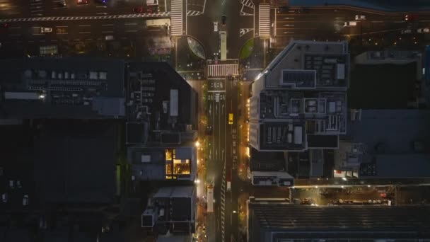 Wysoki kąt widzenia podświetlanych ulic i budynku w nowoczesnej dzielnicy miejskiej w nocy. Pojazdy przejeżdżające przez skrzyżowania. Kioto, Japonia. - Materiał filmowy, wideo
