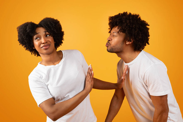 Friendzone Concept. Disgusted black woman avoiding unwanted kiss from obsessed man in love who trying to reach her and pulling lips. Angry young lady refusing and showing stop gesture with palms - Photo, Image