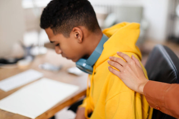 A moment of empathy, as a hand offers comfort to a young person in distress, while at a desk with papers - Photo, Image
