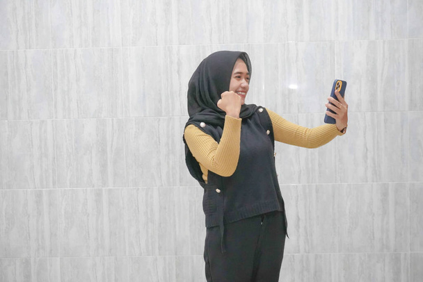 Uitdrukking van een Aziatische Indonesische vrouw met een zwarte hijab met gele mouwen - Foto, afbeelding