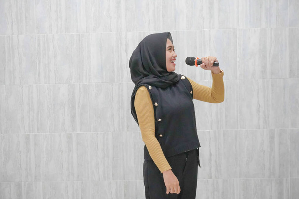 Expression of an Asian Indonesian woman wearing a black hijab with yellow sleeves - Photo, Image