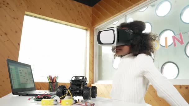 Creatief gelukkig meisje draagt VR-headset en kijkt rond in metaverse. Grappig kind genieten van het invoeren van virtuele wereld programma in STEM-technologie klasse met auto model en draden op tafel. Erutie. - Video