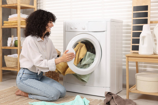 Woman putting laundry into washing machine indoors - Фото, изображение