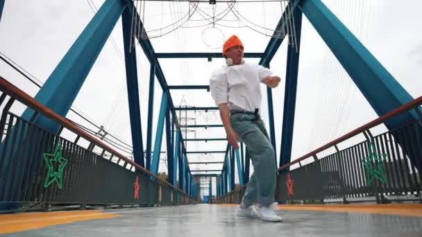Professionelle Breakdancer führen Streetdance-Schritte an der Brücke auf. Asiatische Hipster tragen Kopfhörer, während sie frieren. Break Dancer, Streetdance Freestyle Konzept. Outdoor-Sport 2024. Schwungvoll. - Filmmaterial, Video