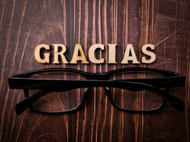 Horní pohled brýle a dřevěné slovo s textem GRACIAS na dřevěném pozadí. - Fotografie, Obrázek