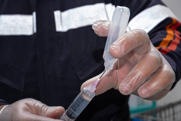 Медсестра в защитной перчатке, удаляет противовоспалительные средства из пластиковой ампулы. - Фото, изображение