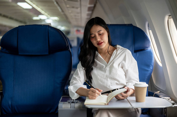Una atractiva y elegante empresaria asiática está en clase ejecutiva en un avión, volando a otra ciudad para una reunión de negocios. conceptos de personas y transporte - Foto, Imagen