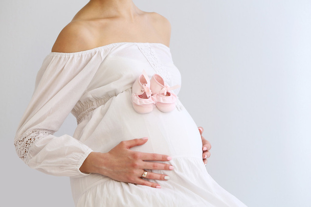 schwangere Frau mit Babystiefeln auf weißem Wandhintergrund - Foto, Bild