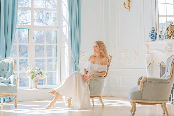 Romantische oude geld stijl. Vrouw draagt witte midi jurk op koninklijke lichtblauwe achtergrond, modieuze scène. Concept van vintage luxe levensstijl. - Foto, afbeelding