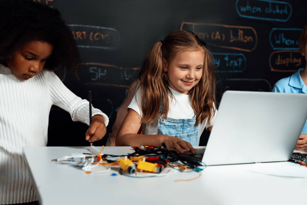 Smart girl in white bib learning about coding robotics technology using laptop in the STEM class. Schoolboy in blue shirt try to educate motherboard while smart schoolgirls reading code. Erudition. - Photo, Image