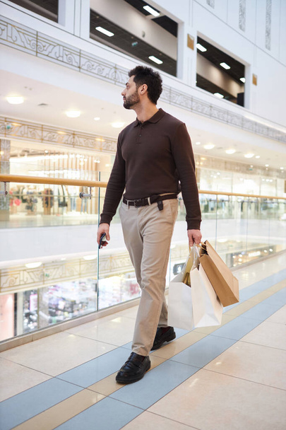Ritratto verticale a figura intera dell'uomo che cammina nel centro commerciale e tiene le borse - Foto, immagini